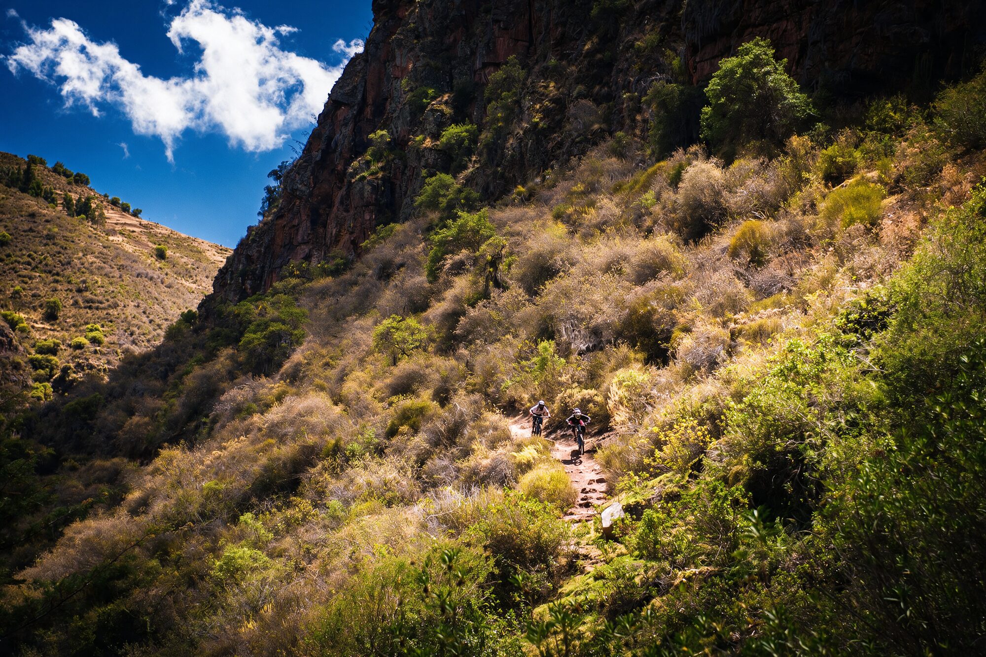 Singletrack cortado en la ladera del cañón, con el cielo del Valle Sagrado arriba